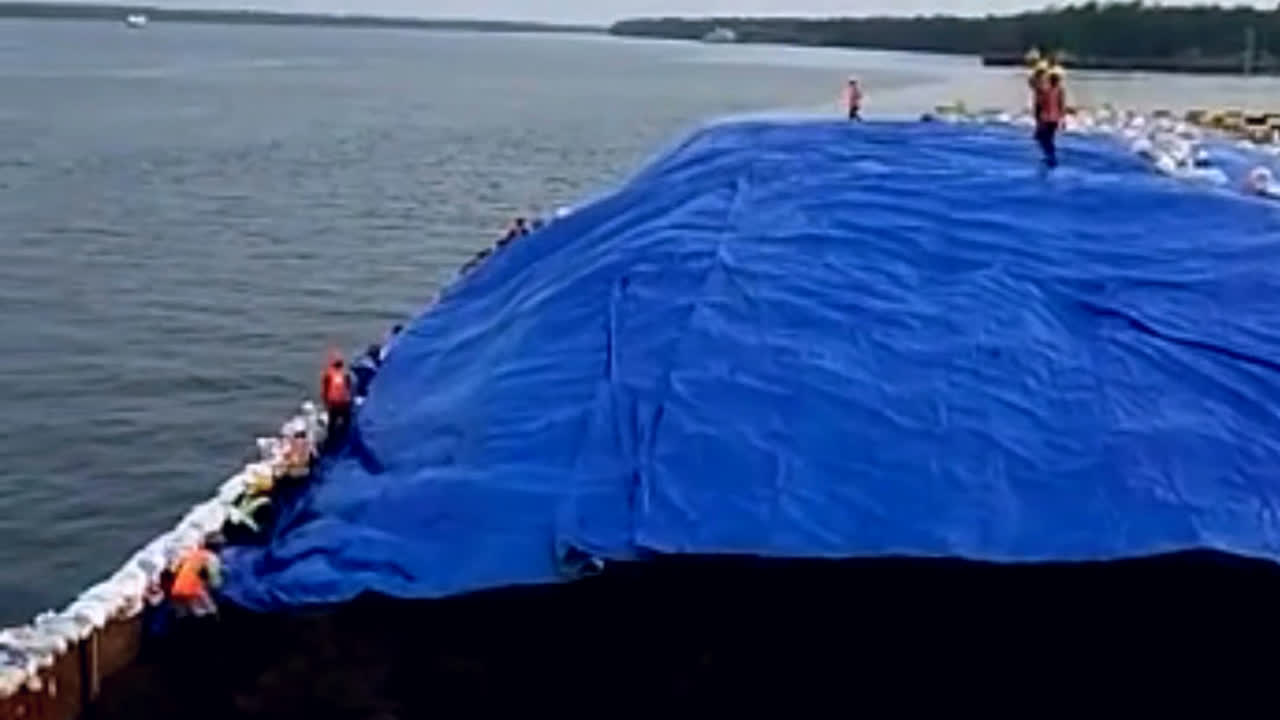 Pekerja berompi oranye menutup muatan batubara di tongkang menggunakan terpal biru